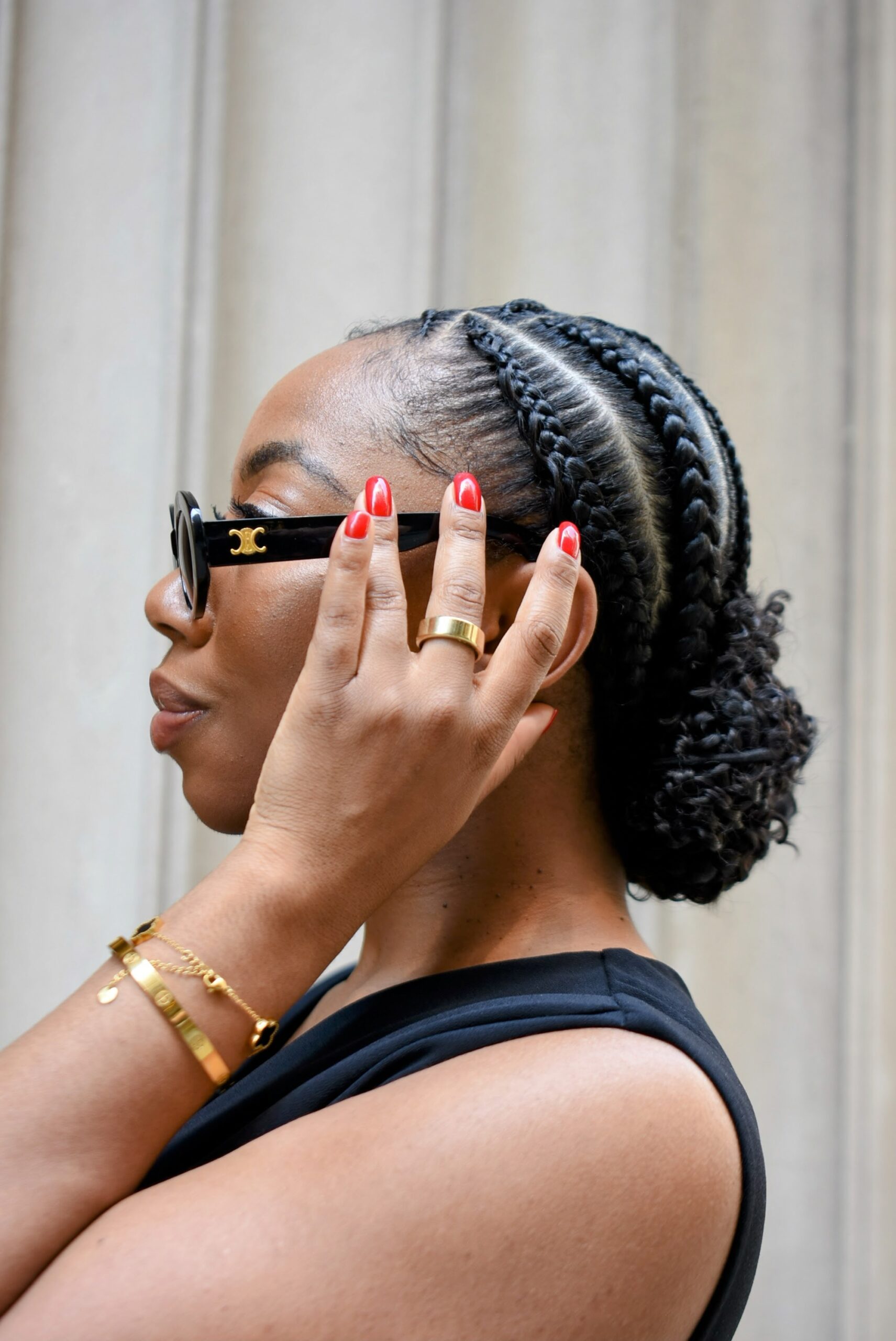 Close-up of a woman wearing a braided updo with a low curly bun, accessorized with gold jewelry, an Oura ring, and red nail polish.