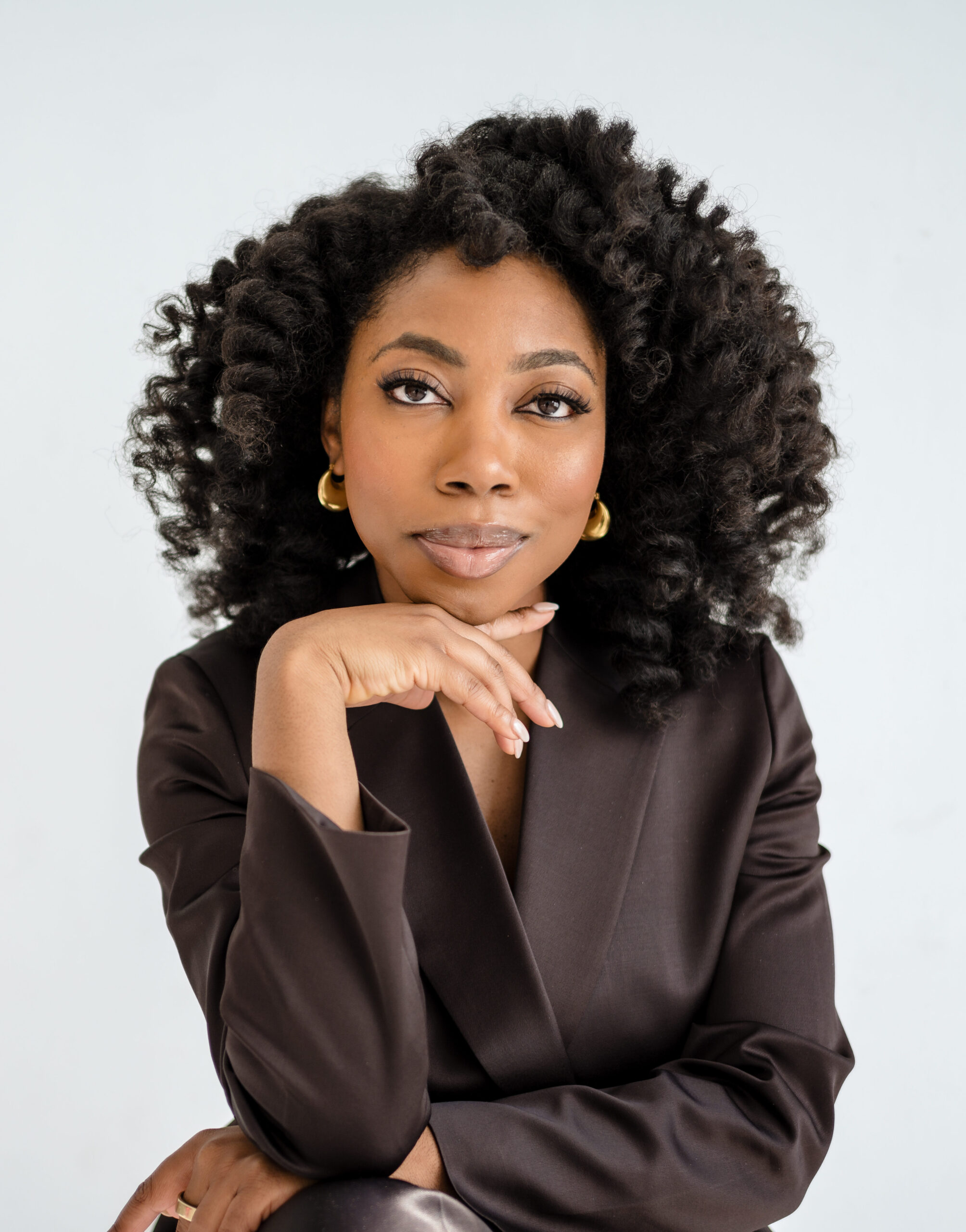 Black woman natural hairstyle afro brown suit hand on chin 