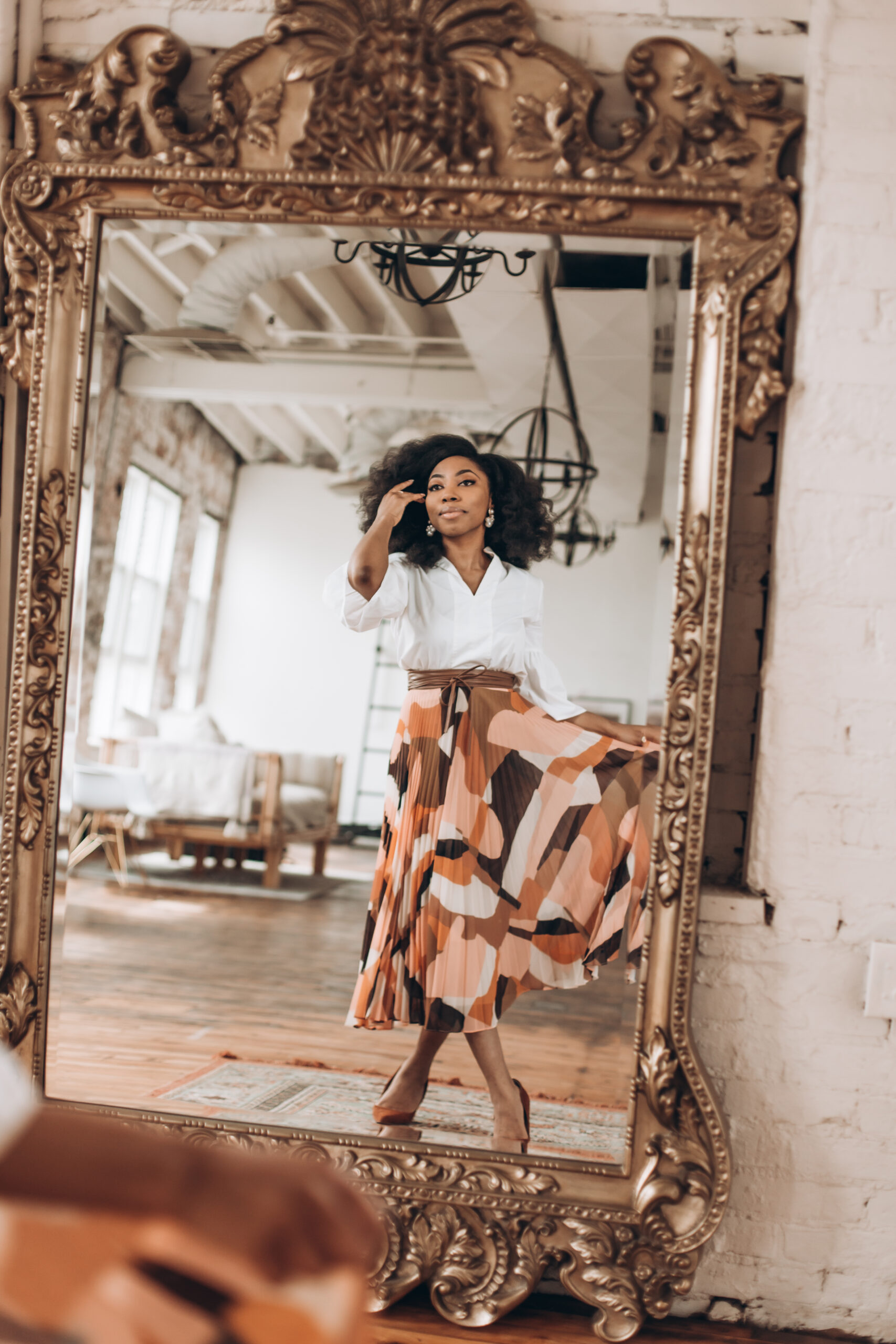 Black woman in business casual staring into a mirror with patterned skirt